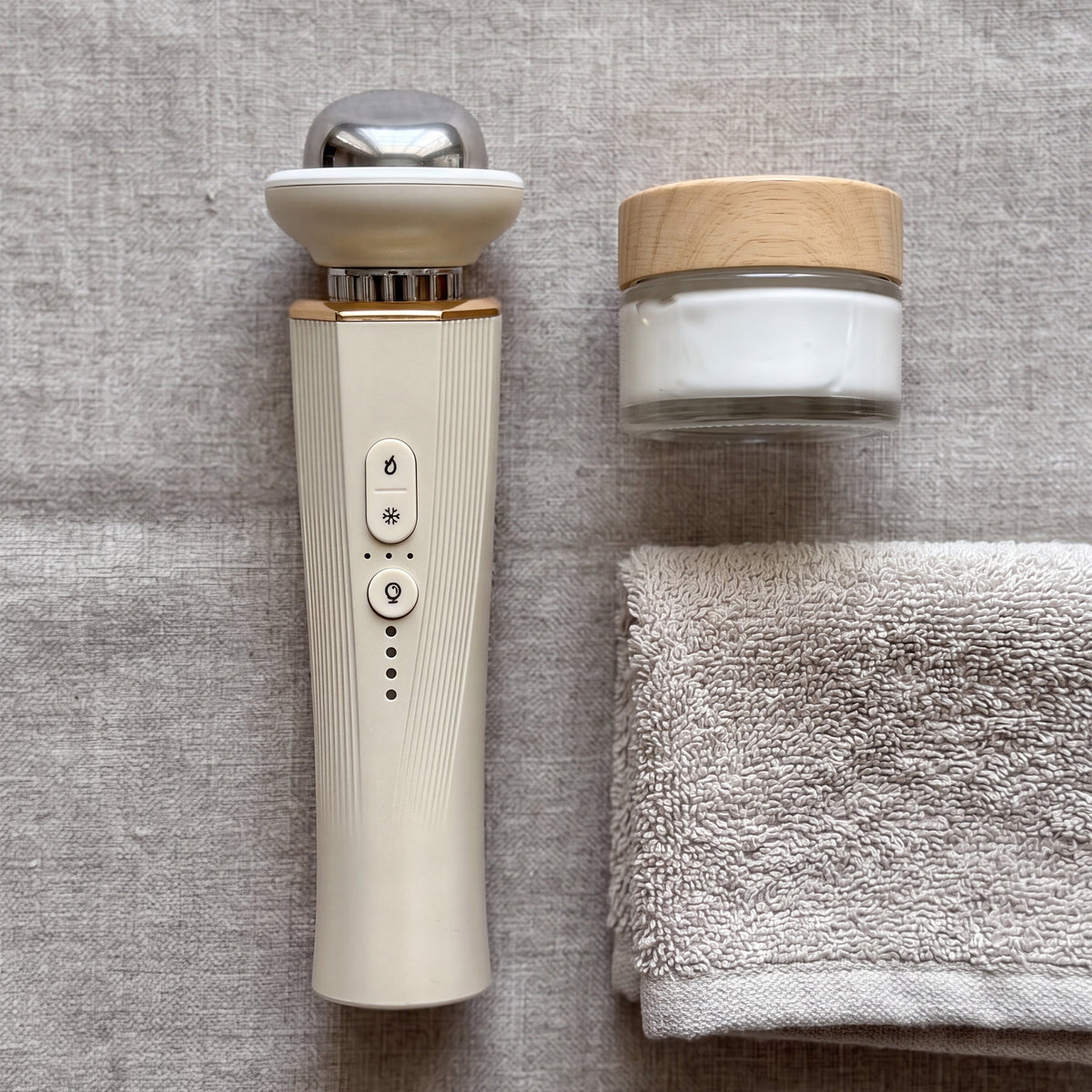 Beauty device, jar of cream, and towel on a textured surface